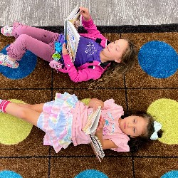 A top-down view of two HPES students reading on the carpet in the library.